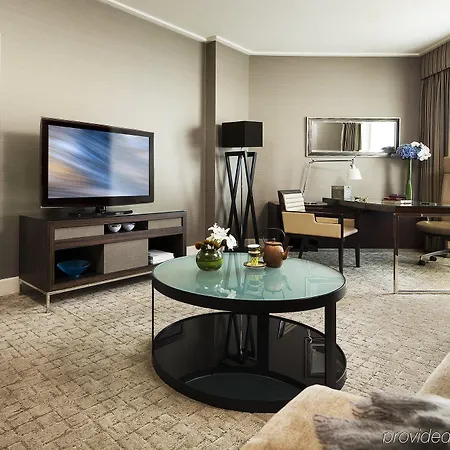 Four Seasons Hotel Sydney Exterior photo The photo showcases an elegantly designed hotel room or suite. 

- **Living Area**: A comfortable sofa is positioned in the foreground, along with a stylish coffee table featuring a glass top and decorative items on it. 
- **Television**: A large fla
