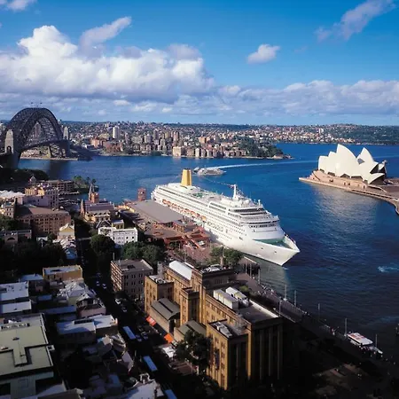 Four Seasons Hotel Sydney Room photo The photo shows a picturesque view of Sydney, Australia. Prominently featured is the iconic Sydney Opera House, known for its unique sail-like design, situated along the shoreline. To the left, the Sydney Harbour Bridge arches over the water, connect